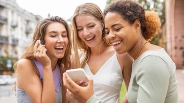 Amigas rindo enquanto olham para tela de celular