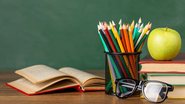 Mesa de professor com livros, lápis, óculos e maçã