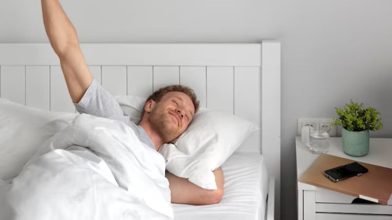 homem deitado na cama, se espreguiçando e sorrindo após acordar