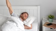 homem deitado na cama, se espreguiçando e sorrindo após acordar