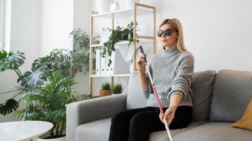 Mulher deficiente visual sentada no sofá enquanto segura uma bengala
