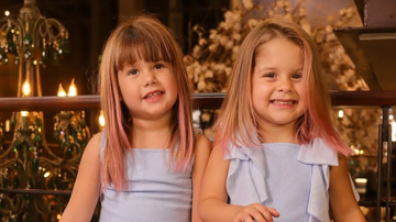 Duas crianças loiras com mechas coloridas nos cabelos sorrindo para a câmera.