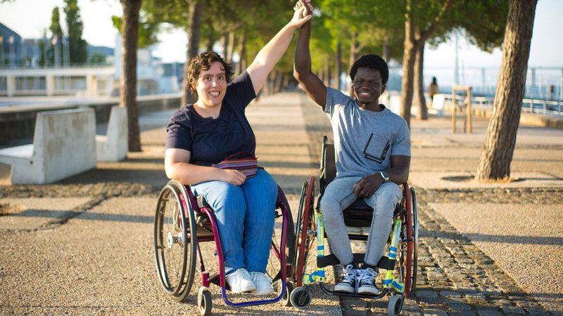 Homem e mulher, cada um em sua cadeira de rodas, na calçada