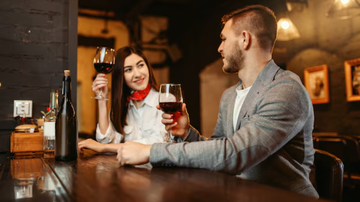 casal flertando sentados em mesa de resturante, segurando taças de vinho