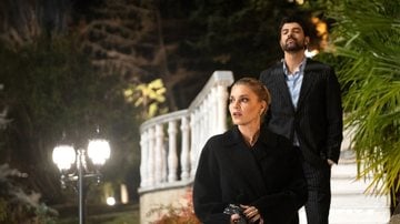 Personagens da novela caminhando em jardim durante a noite.
