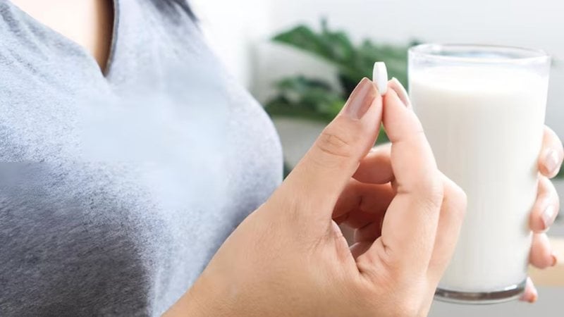 mulher segurando remédio com uma mão e copo de leite com a outra.