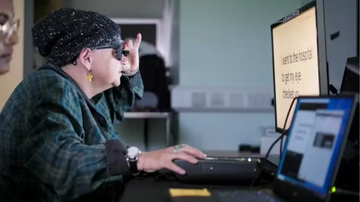 Idosa fazendo uso de nova tecnologia para a visão em frente à tela de computador