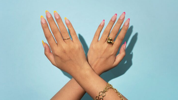 Unhas no estilo francesinha em cores distintas, dispostas sob fundo azul neutro.