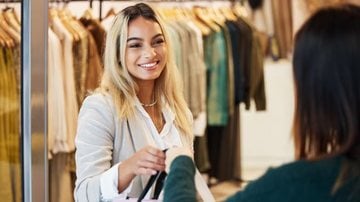 vendedora entregando sacola para cliente na porta de loja