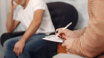 homem sentado conversando com sua psicóloga, que está anotando informações em papel.