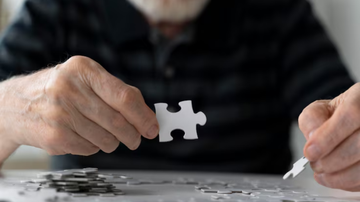 Idoso com peça de quebra-cabeças em mãos.