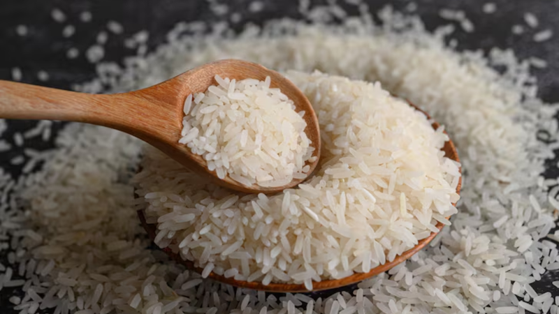 Colher cheia de arroz, sob pote com grãos de arroz acumulados.