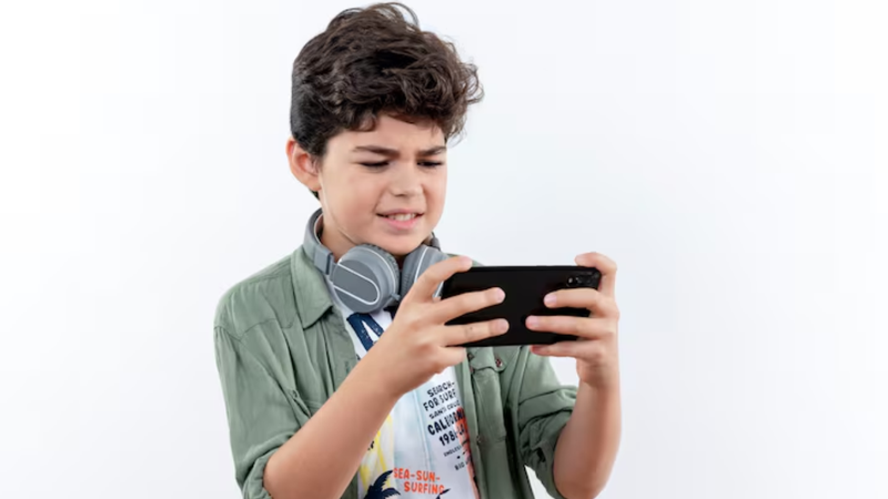 Criança sob fundo branco utilizando aparelho de celular para jogar.