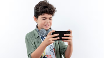 Criança sob fundo branco utilizando aparelho de celular para jogar.