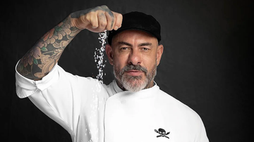 Chef Henrique Fogaça posando sob fundo neutro e despejando sal com a ponta dos dedos