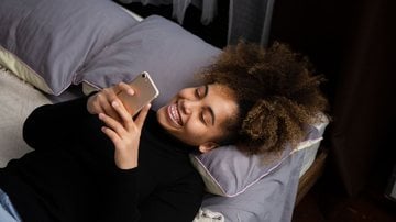 mulher deitada na cama com celular na mão mandando mensagem de boa noite