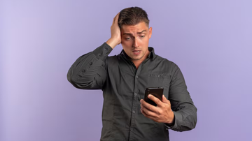 homem frustrado olhando para o celular sob fundo roxo.