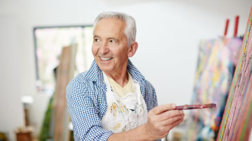 Idoso posando enquanto pinta quadro.