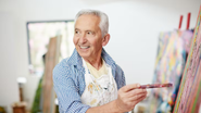 Idoso posando enquanto pinta quadro.