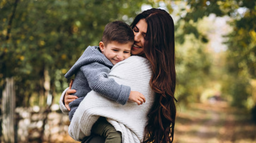 Mão e filho se abraçando com árvores ao fundo.