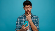 Homem com o celular nas mãos e expressão de dúvida.