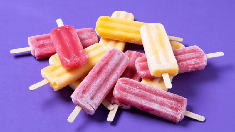 Picolés de distintos sabores dispostos em cima de fundo roxo.