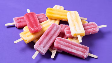 Picolés de distintos sabores dispostos em cima de fundo roxo.