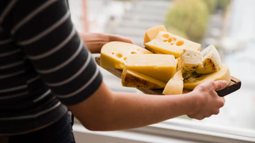 Indivíduo carregando bandeja cheia de queijos.