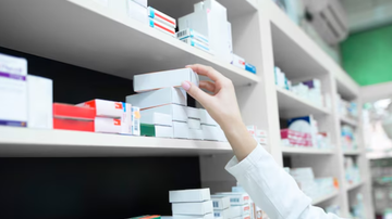 Indivíduo pegando caixa de remédio em prateleira.