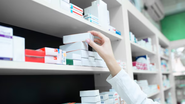 Indivíduo pegando caixa de remédio em prateleira.