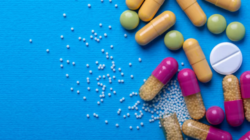 Pílulas e cápsulas de medicamentos dispostos sub fundo azul.