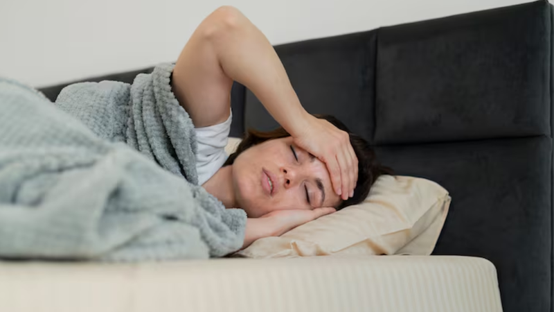 Mulher deitada em sua cama, acordando, demonstrando sinais de cansaço.