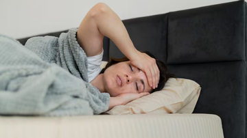 Mulher deitada em sua cama, acordando, demonstrando sinais de cansaço.