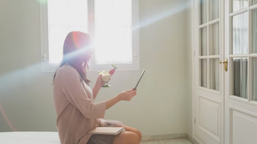 Mulher tomando sol em quarto de sua casa.