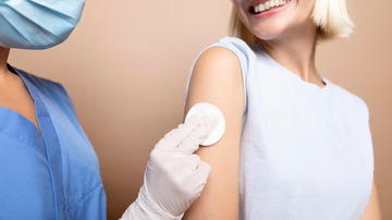 Mulher sorridente após receber dose de vacina das mãos de profissional da saúde.