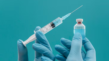 Profissional da saúde segurando seringa e recipiente com líquido contendo imunizante.