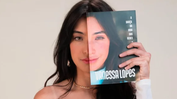 Vanessa Lopes, posando sob fundo neutro, segurando o seu livro em frente ao seu rosto.