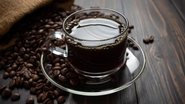 xícara de café disposta ao lado de grãos