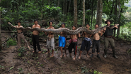 Homens carregando cobra selvagem em meio à mata.