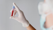 indivíduo segurando tubo de ensaio com amostra de sangue.
