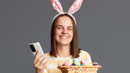 Mulher com celular na mão e ovos de chocolate em outra.