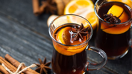 Copo de quentão com anis estrelado, pau de canela e rodela de laranja.