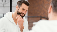 homem se olhando ao espelho sorridente, enquanto cuida de sua barba.