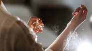 Mulher segurando frasco de perfume e borrifando a fragrância.