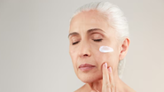 mulher de mais de 50 anos passando creme no rosto