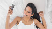 mulher acordando, olhando o celular e sorrindo.