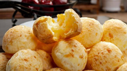 Pães de queijo empilhados sob prato em bancada de cozinha.