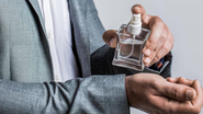 homem de terno aplicando perfume em seu pulso.
