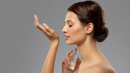 mulher aplicando perfume e cheirando o próprio pulso, desfrutando da fragrância.