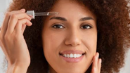 Mulher fazendo skincare, sorrindo e prestes a aplicar serum em seu rosto.